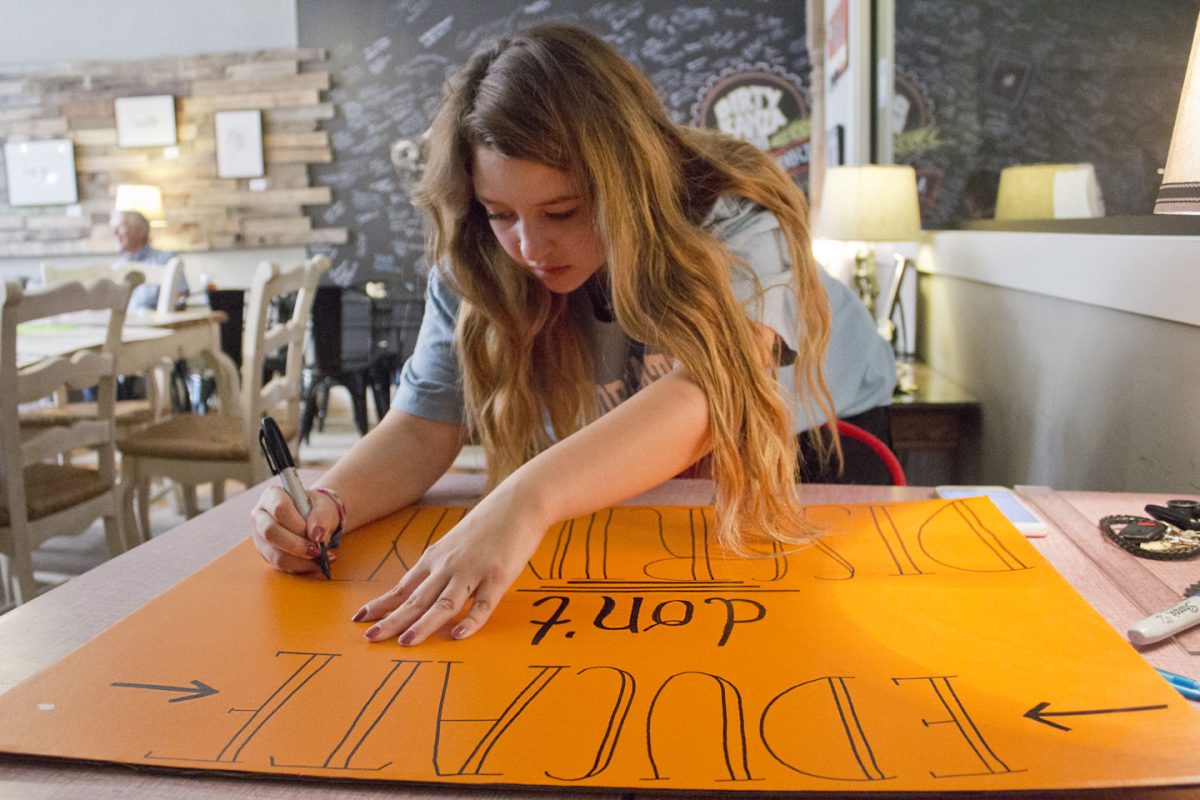 Aleana Cuevas-Montagne, sophomore undecided major, works on a poster that reads &#8216;educate don&#8217;t discriminate&#8217; last Monday at Gravel City Roasters, 608 Commercial St. The poster was made for the rally in support of dreamers held last Tuesday.