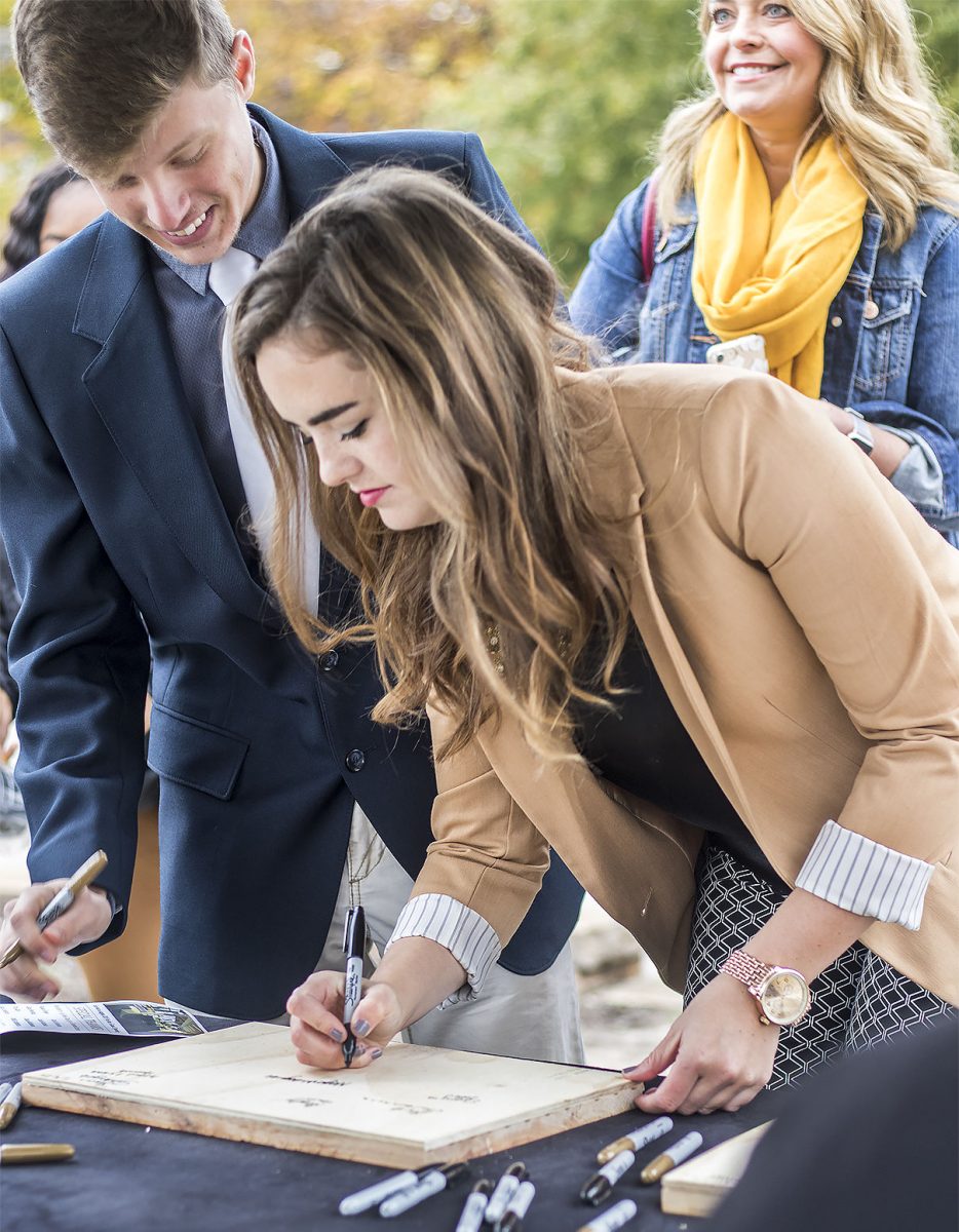 Megan McReynolds, associated student government president and junior sociology major, and Jacob Miller, ASG vice president and sophomore communication major, sign pieces of wood that will be hidden in the new dorms. The groundbreaking ceremony took place on Saturday in the parking lot across from King Hall.