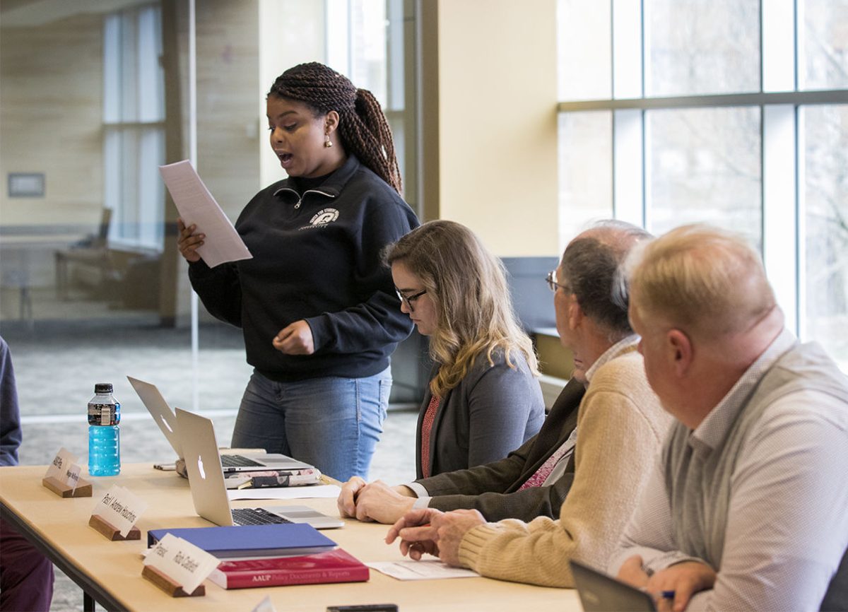 Kayla Gilmore, senior political science major, reads from a statement about the importance of the diversity, equity and inclusion bill presented for first reading in the Faculty Senate meeting Tuesday in the Skyline Room in Memorial Union. The bill would require faculty to include a diversity statement in their syllabi.&#160;