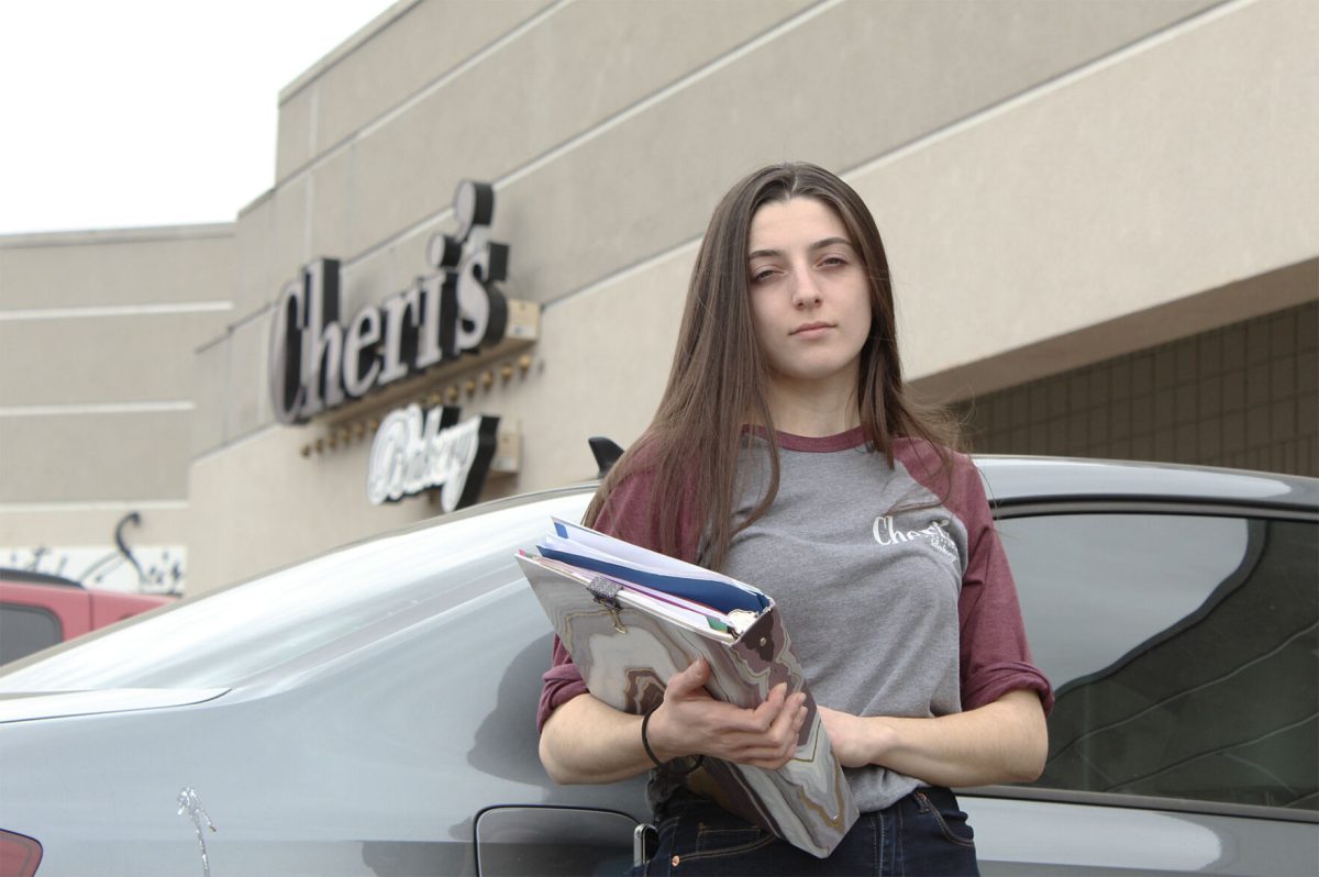 Kaitlynd Brasher stands against her 2016 Volkswagen with a binder full of notes and documents regarding her student debt in front of Cheri&#8217;s Bakery, 2121 on North Tyler Road #300, Wichita, April 11. Brasher has recently been sued by Emporia State for &#8220;unearned financial aid&#8221; resulting in years of debt and her wages being garnished at the bakery. &#160;